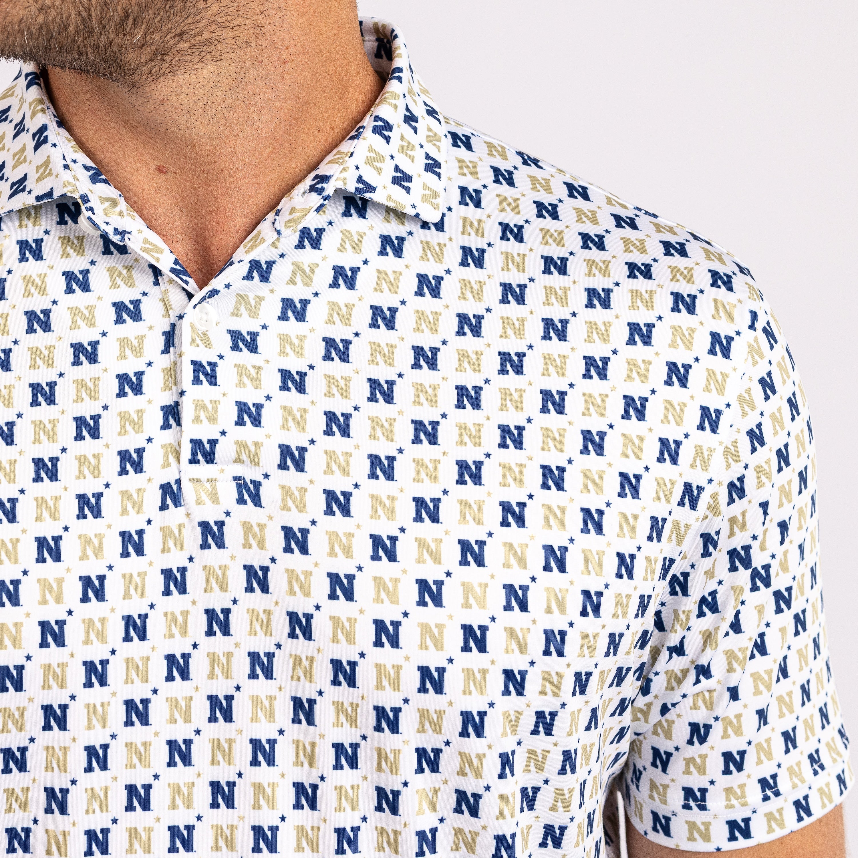 Close-up of a man wearing a short-sleeve collared polo shirt with an allover repeating 'N' logo pattern in navy blue and beige on a white base.