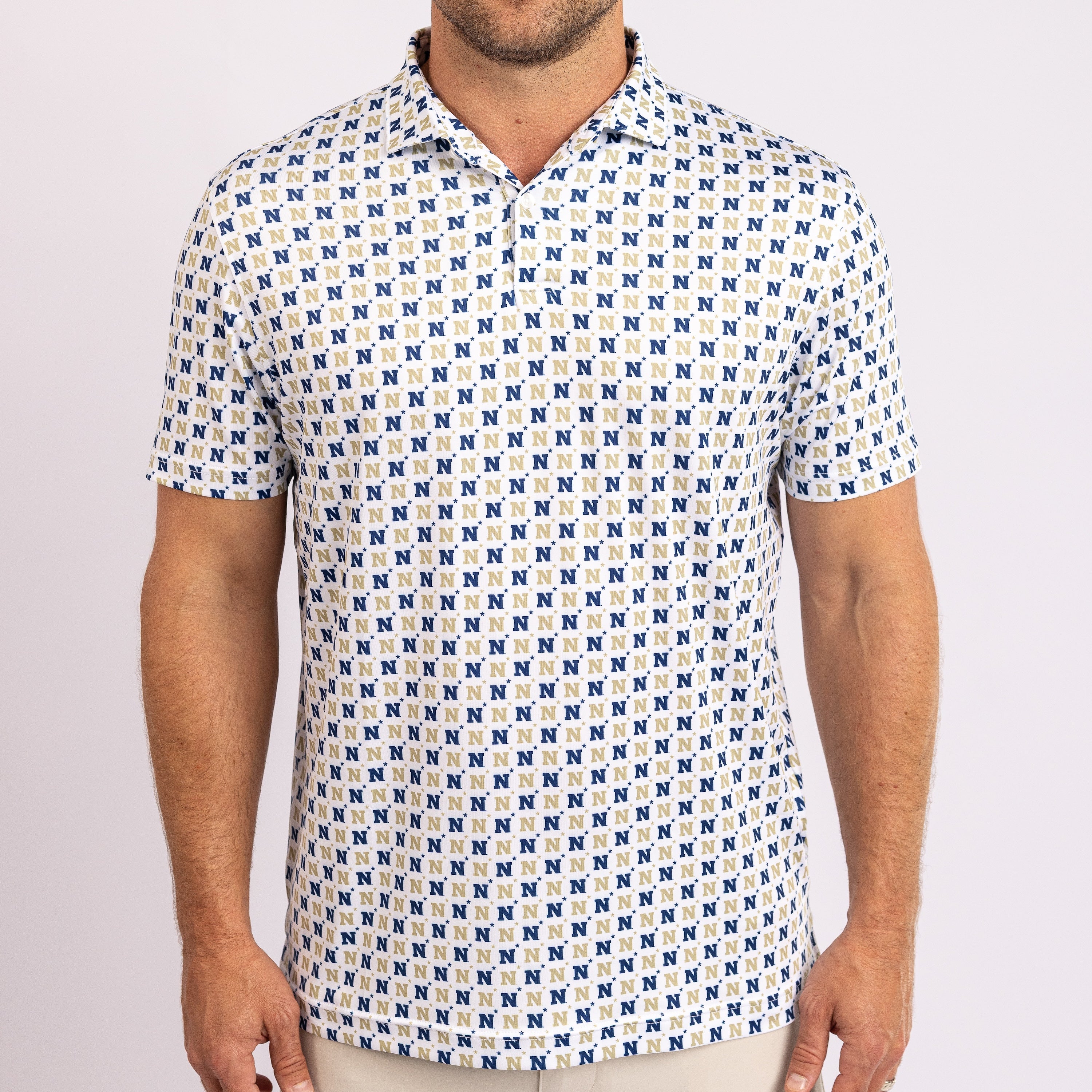 A man wearing a short-sleeve polo shirt with an all-over repeating blue and beige monogram pattern on a white base, shown from the neck to the waist against a light gray studio background.