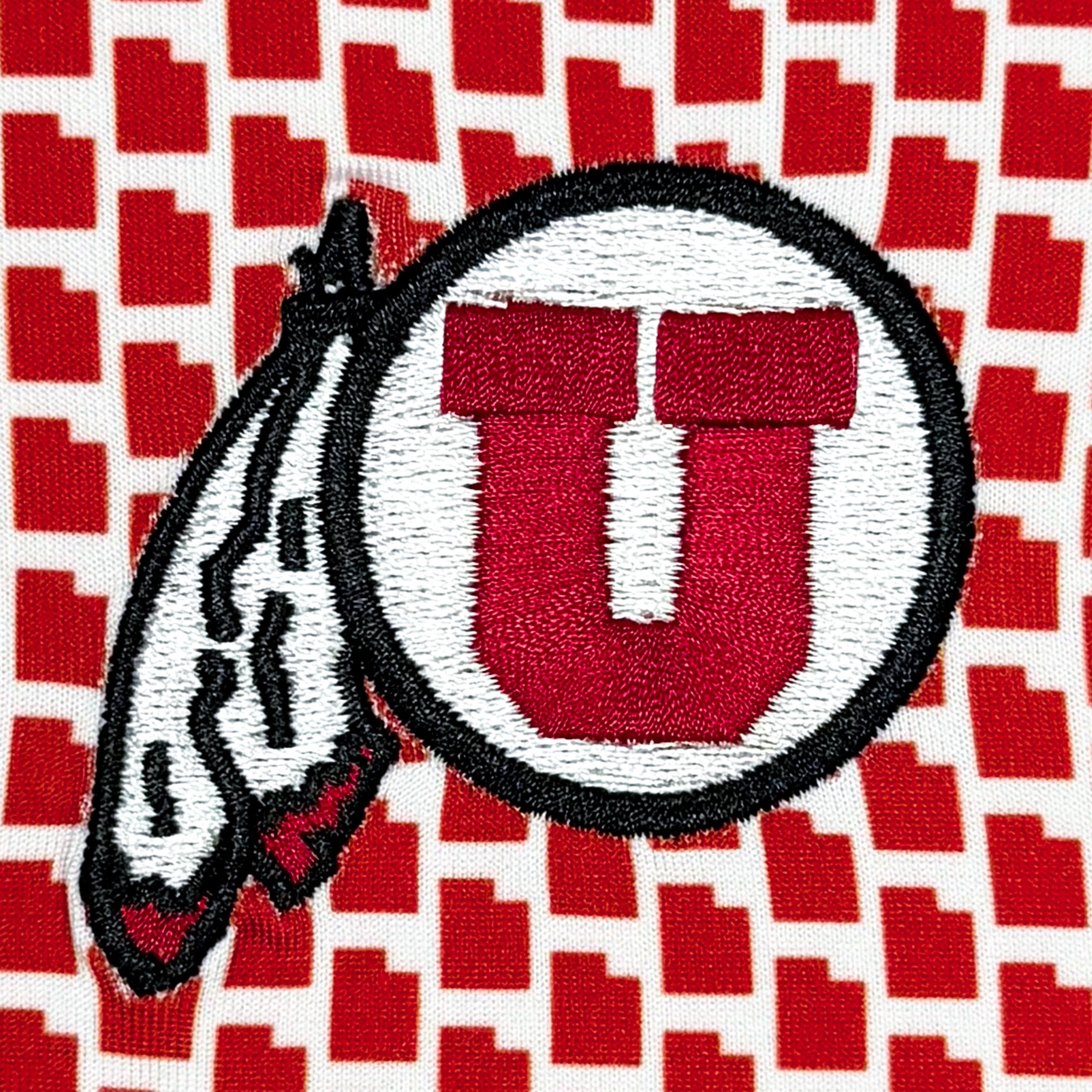 Embroidered circular logo patch featuring a red and white letter U with a feather detail, set against a red and white patterned fabric background.