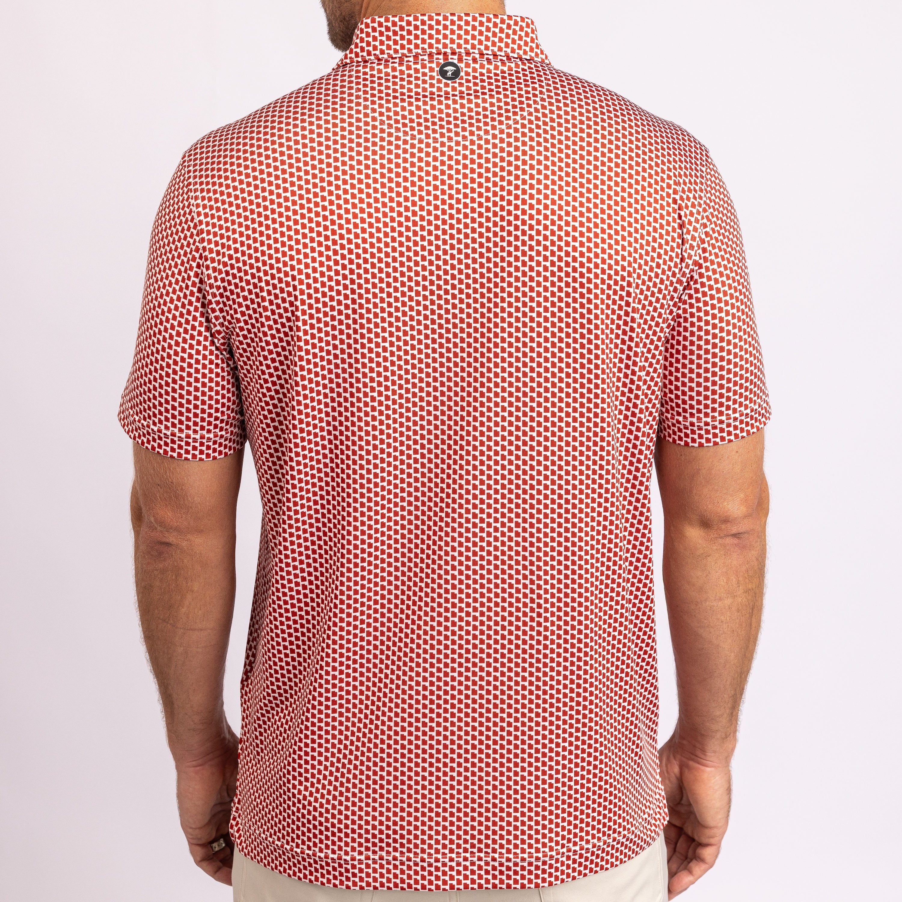 A man viewed from the back wearing a short-sleeve polo shirt with a dense red and white geometric pattern, paired with light beige pants against a plain white studio background.