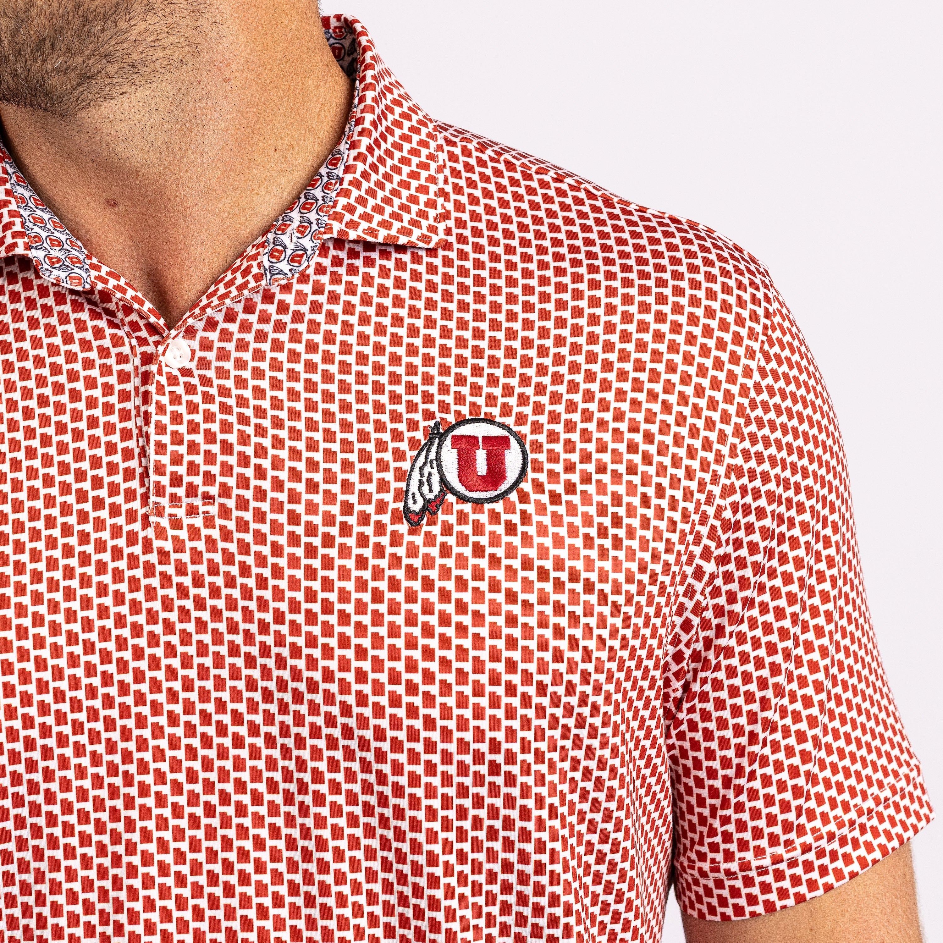 Close-up of a man wearing a short-sleeve polo shirt with a red and white geometric pattern and a circular Utah U logo patch on the chest.